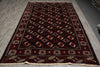 Load image into Gallery viewer, A rectangular dark red and black patterned rug with cream and red motifs, laid flat on a gray wood floor.