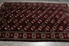 Load image into Gallery viewer, A large rectangular area rug laid flat on a gray tiled floor, featuring a dark red and black background with repeating cream and red geometric motifs and ornate borders.