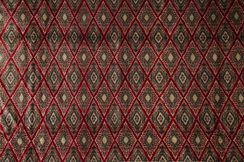 A close-up of a woven textile with a repeating diamond pattern in red, black, and beige.