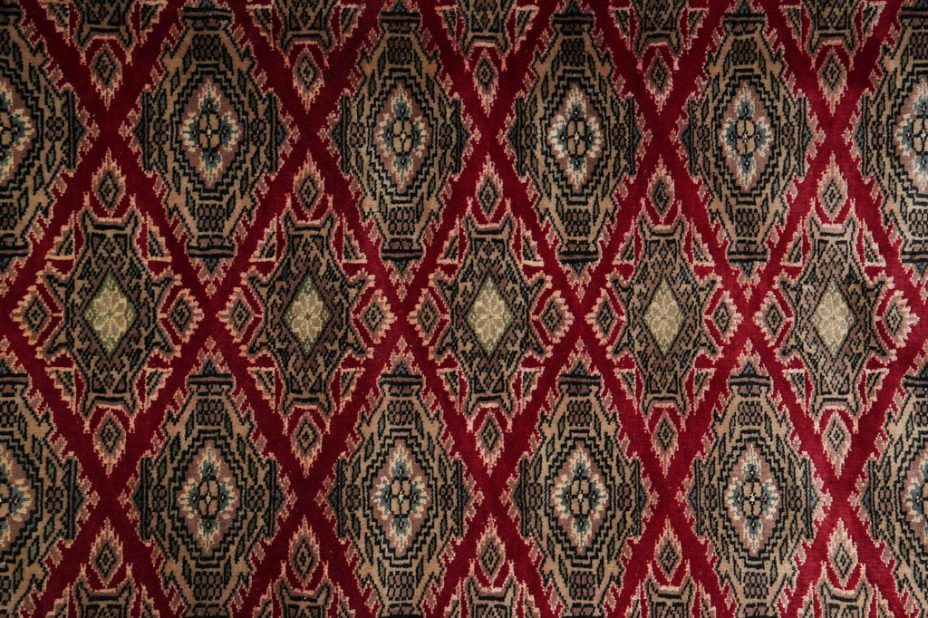 A close-up of a patterned rug or textile with a repeating diamond motif in deep red, black, beige, and muted gold tones.