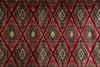 Load image into Gallery viewer, A close-up of a patterned rug or textile with a repeating diamond motif in deep red, black, beige, and muted gold tones.