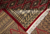 Load image into Gallery viewer, A close-up of a patterned area rug showing its corner, with cream fringe, a deep red border, and a beige field with black geometric motifs over a red background.
