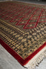 Load image into Gallery viewer, A traditional patterned rug with red borders, beige and black geometric motifs, and cream fringe, shown laid out on a gray floor.