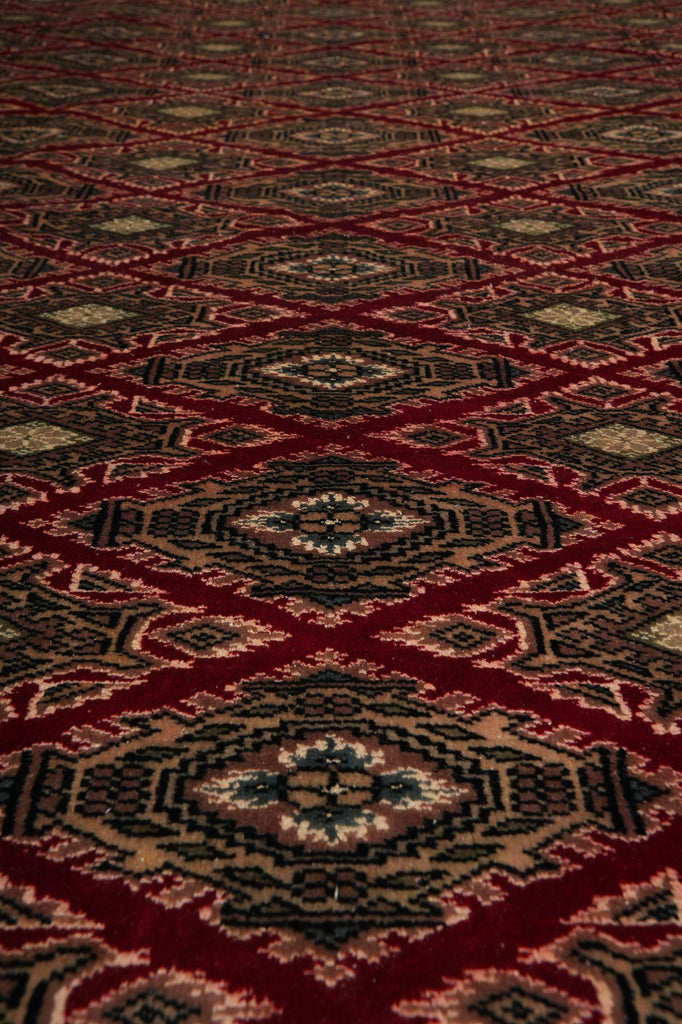 A close-up of a patterned rug or textile with repeating diamond motifs in deep red, black, beige, and muted blue-gray tones.