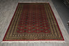 Load image into Gallery viewer, A rectangular area rug with a traditional geometric pattern, featuring a deep red central field, a dark brown border, and cream accents, laid out on a gray wood floor.