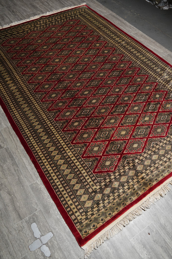 A rectangular patterned area rug with cream, red, and dark brown geometric designs, laid out on a gray tiled floor.