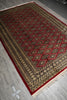 Load image into Gallery viewer, A rectangular patterned area rug with cream, red, and dark brown geometric designs, laid out on a gray tiled floor.