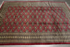Load image into Gallery viewer, A rectangular area rug with a traditional geometric pattern, featuring red diamond motifs over a beige and brown background with a red border.