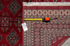 Load image into Gallery viewer, A close-up of a patterned area rug with a red border and cream fringe, shown alongside a yellow tape measure and a white size tag on a gray floor.