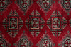 Load image into Gallery viewer, A close-up of a red patterned rug with repeating geometric medallion motifs in black, beige, and muted blue-green.