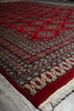 Load image into Gallery viewer, A red patterned area rug with cream and black geometric borders and fringe, photographed laid out on a light gray floor.