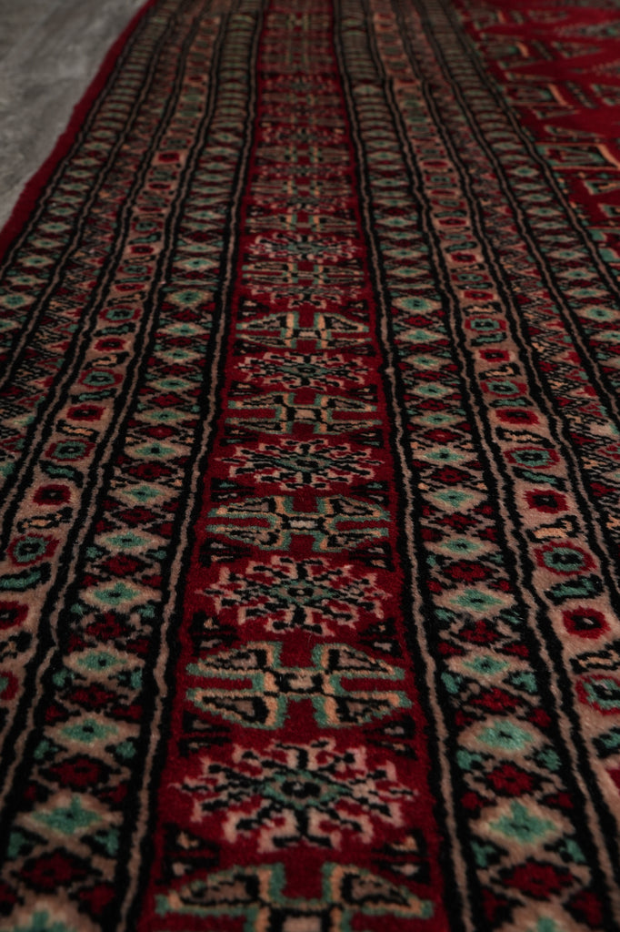 A close-up view of a traditional patterned rug with horizontal bands of red, black, beige, and turquoise geometric motifs.