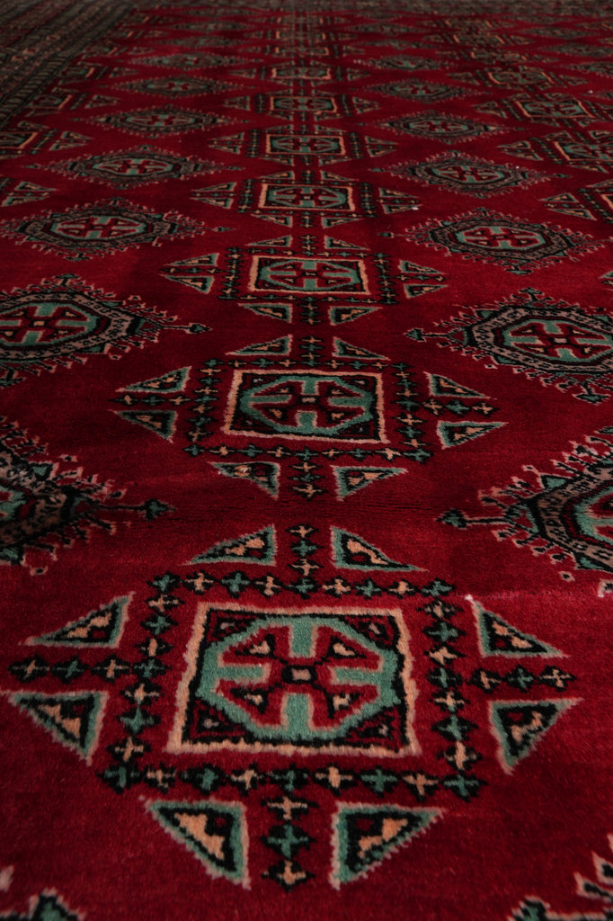 A close-up of a red patterned rug with geometric motifs in black, beige, and light blue.