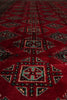 Load image into Gallery viewer, A close-up of a red patterned rug with geometric motifs in black, beige, and light blue.
