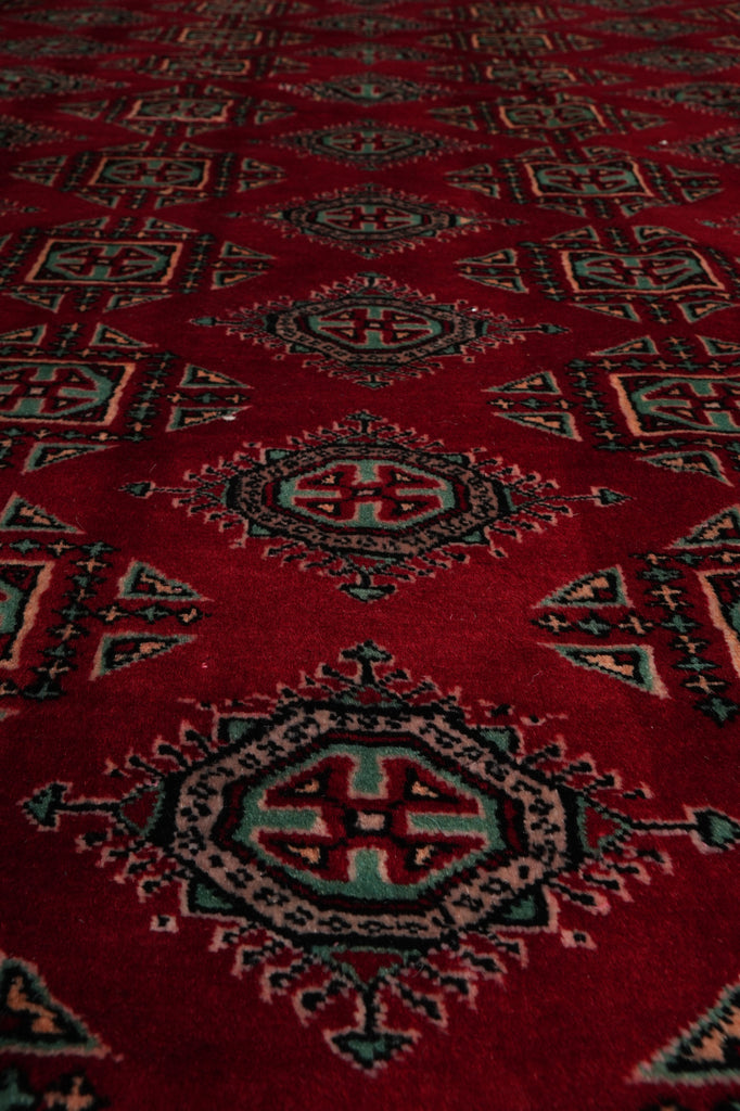 A close-up of a red patterned rug with traditional geometric medallions in black, green, and beige.
