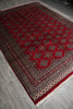 Load image into Gallery viewer, A traditional Persian-style area rug with a deep red field, intricate geometric and diamond patterns in black, beige, and white, and a matching red border, shown laid out on a gray tiled floor.
