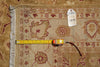Load image into Gallery viewer, A close-up of a patterned area rug in beige and rust tones with a white fringed edge, shown with a yellow tape measure and a small inventory tag on top.
