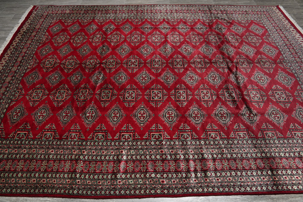 A large red oriental area rug with a detailed geometric diamond pattern and a decorative border, laid flat on a gray wood floor.