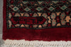 Load image into Gallery viewer, Close-up of a patterned rug corner showing a deep red field, a dark border with beige and teal motifs, and a cream fringed edge.