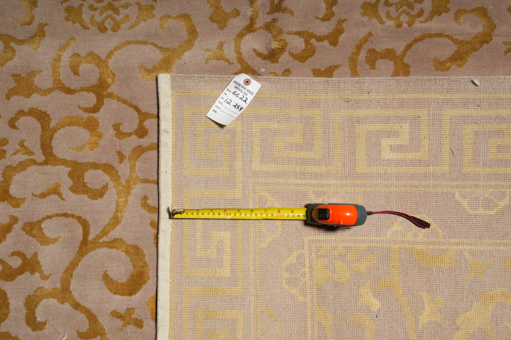 A beige area rug with a yellow Greek key pattern and a white border, shown with a yellow tape measure and a white tag on top of it, placed next to a matching patterned rug.
