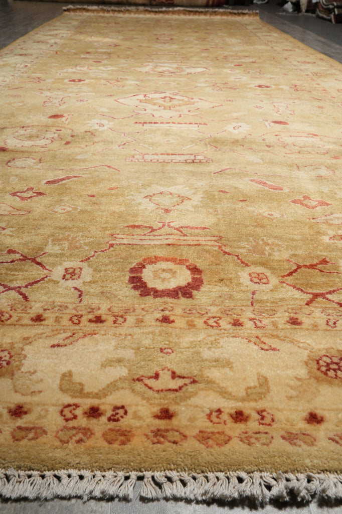 A long rectangular area rug with a distressed traditional pattern in beige, cream, and muted red, featuring a fringed edge and photographed from a high angle.