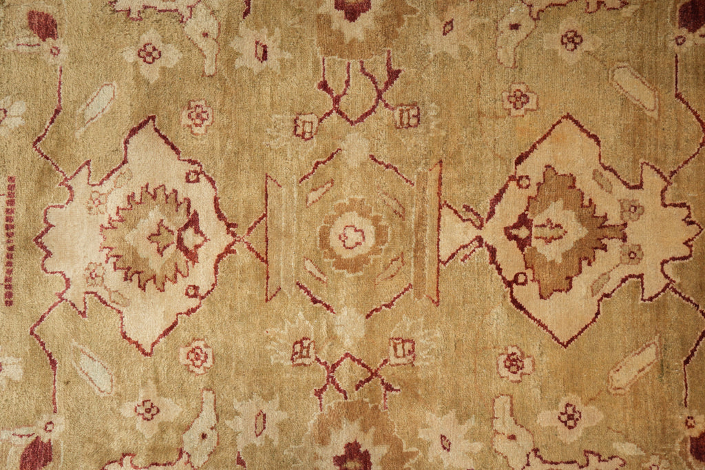A close-up of a vintage-style area rug with a faded beige and tan background, featuring traditional geometric medallions and floral motifs in muted rust red and brown.