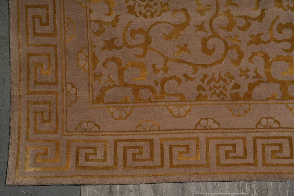 Close-up of a patterned area rug corner showing a beige and gold floral design with a Greek key border on a gray floor.