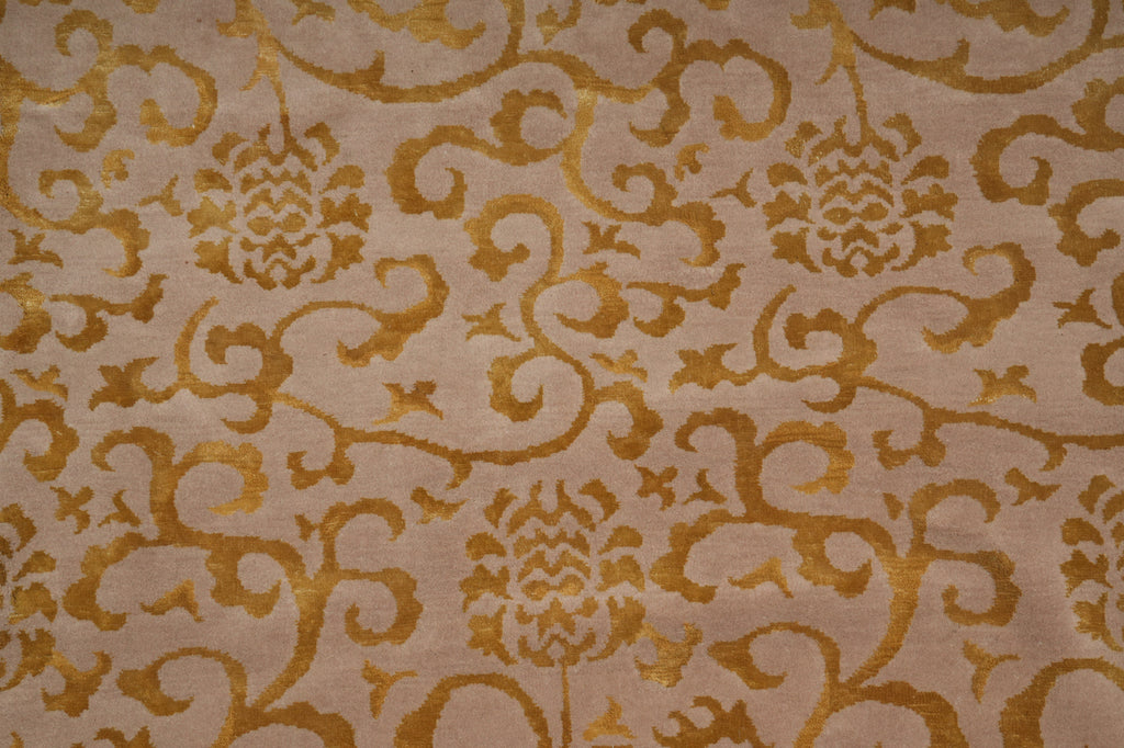 A close-up of a woven fabric with a repeating damask pattern in warm gold on a light beige background.
