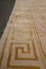 Load image into Gallery viewer, Close-up of a beige textile or rug with a metallic gold Greek key pattern and decorative border details.