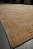 Load image into Gallery viewer, A beige area rug with a gold Greek key border and ornate floral pattern, shown laid out on a gray concrete floor.