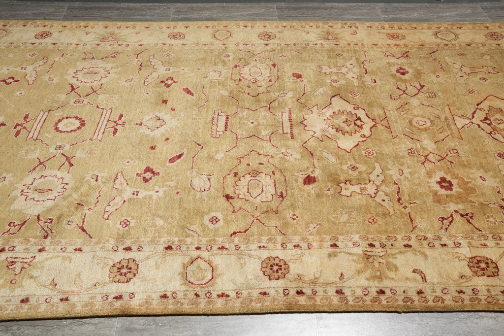 A rectangular area rug with a traditional oriental design, featuring a warm beige background with red and cream patterns, laid out on a gray tiled floor.