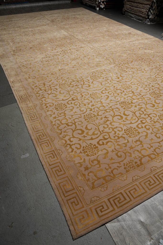 A large rectangular area rug with an ornate traditional floral pattern and Greek key border, shown laid out on a warehouse floor.