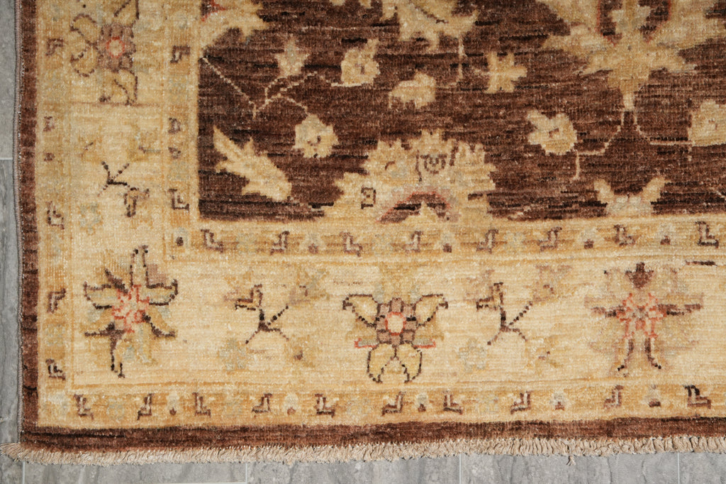 A close-up of an antique-style rug showing its woven border and floral motifs in shades of beige, brown, and muted red.