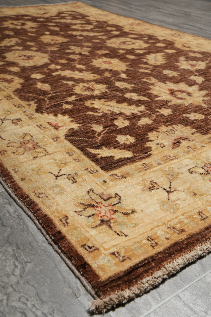 A close-up of a traditional patterned area rug with a beige and brown floral design, shown on a gray tiled floor.