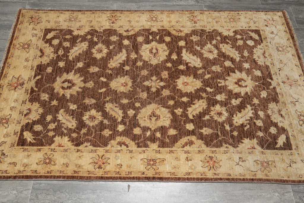 A rectangular area rug with a traditional floral pattern, featuring a dark brown center field and a beige border, laid out on a gray tiled floor.
