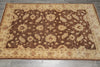 Load image into Gallery viewer, A rectangular area rug with a traditional floral pattern, featuring a dark brown center field and a beige border, laid out on a gray tiled floor.