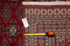 Load image into Gallery viewer, A patterned area rug laid flat on a white surface, shown with a measuring tape and a size tag to indicate dimensions. The rug has a deep red field with cream, beige, and black geometric motifs and borders.