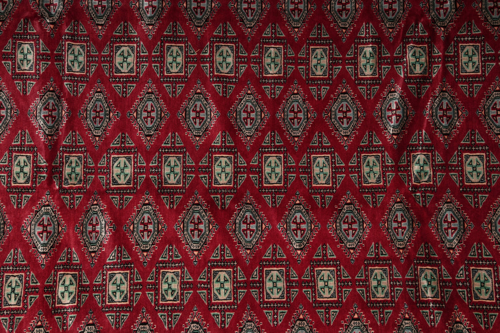 A close-up of a red patterned fabric with repeating diamond and cross motifs in beige, green, and black.