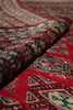 Load image into Gallery viewer, A close-up of a folded red patterned rug showing detailed traditional motifs in black, beige, and light green.