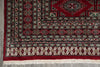 Load image into Gallery viewer, A close-up of a traditional patterned rug corner, showing a deep red field, geometric borders, and cream fringe on a gray floor.
