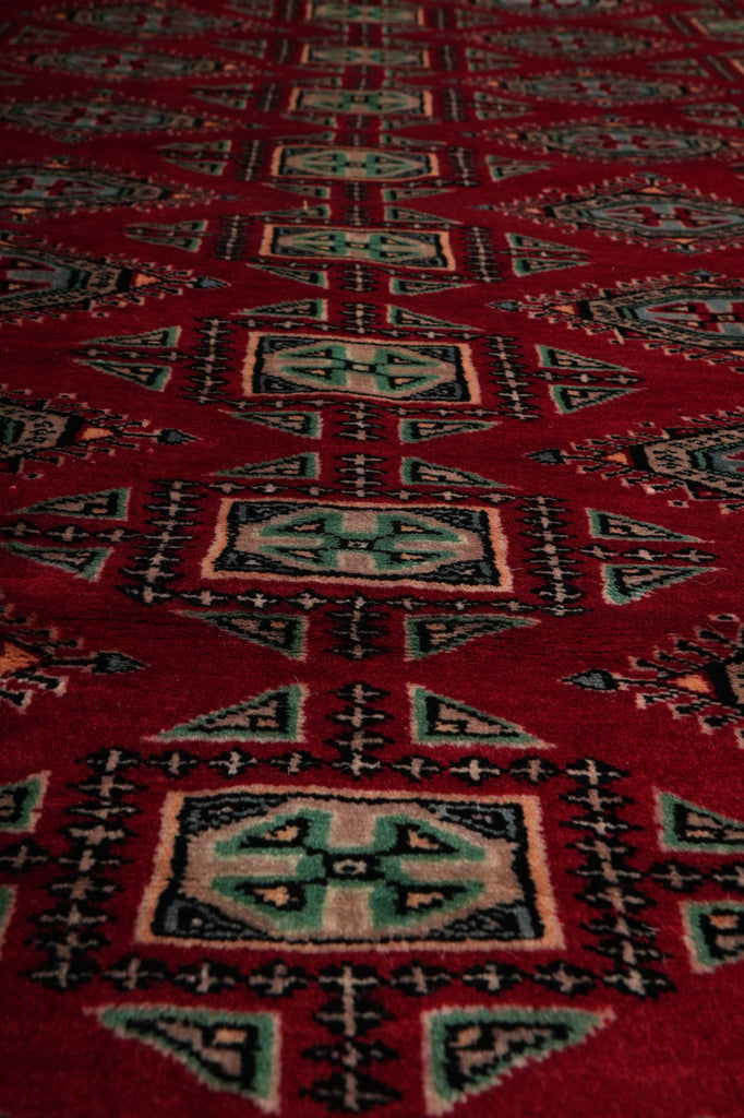 A close-up of a red patterned rug with geometric motifs in beige, black, and teal.