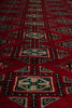 Load image into Gallery viewer, A close-up of a red patterned rug with geometric motifs in beige, black, and teal.