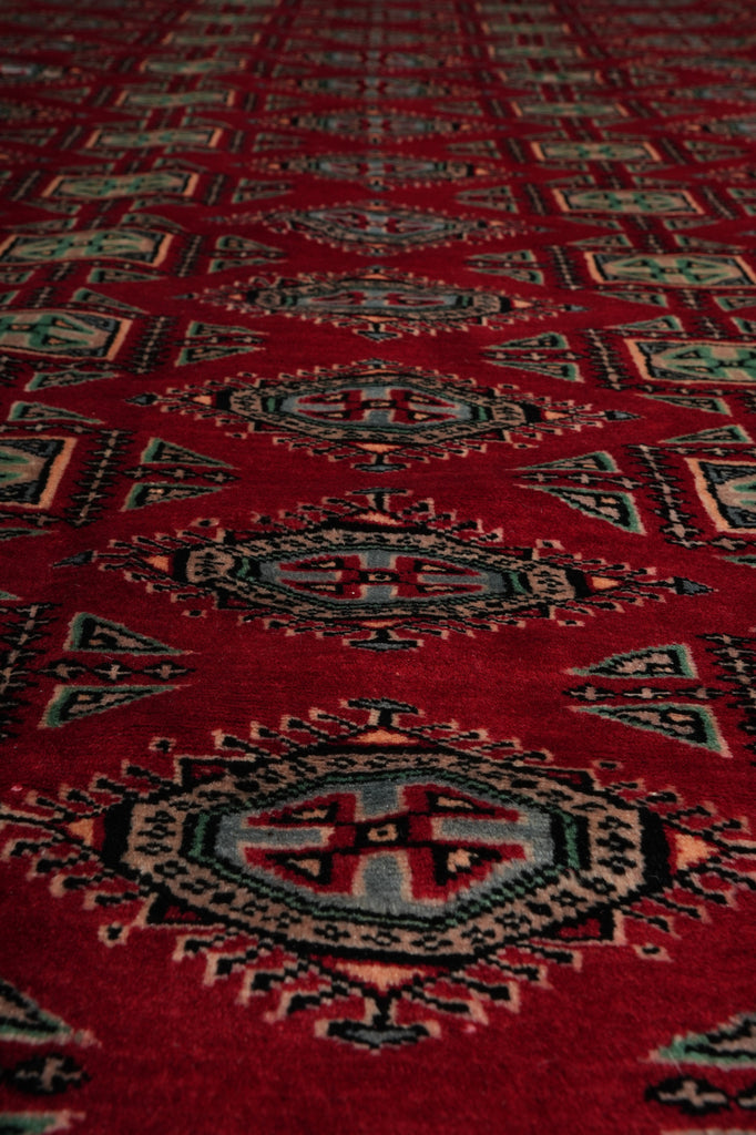 A close-up of a red patterned rug with geometric and tribal-style motifs in black, beige, and muted green.