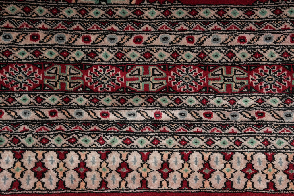 A close-up of a patterned rug with horizontal bands of geometric and floral motifs in red, black, beige, and light blue.