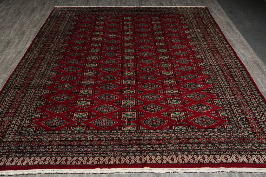 A traditional Persian-style area rug with a deep red field, featuring a repeating diamond pattern in beige, black, and green, bordered by ornate red and beige patterns, laid out on a gray tiled floor.