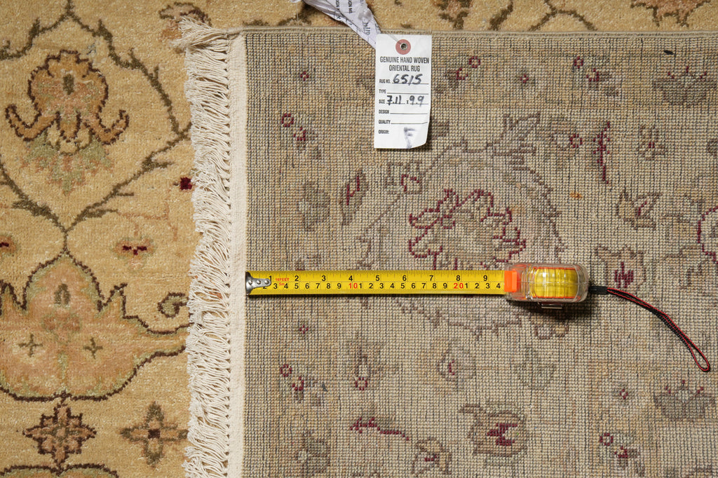 A close-up of a patterned area rug with cream fringe, shown with a yellow tape measure and a white inventory tag on top.