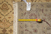 Load image into Gallery viewer, A close-up of a patterned area rug with cream fringe, shown with a yellow tape measure and a white inventory tag on top.