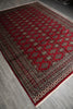 Load image into Gallery viewer, A traditional oriental area rug with a deep red field, featuring a repeating diamond pattern and ornate borders in beige, brown, and black, laid out on a gray tiled floor.