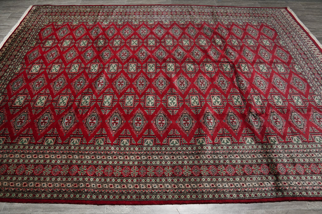 A large traditional oriental rug with a red diamond pattern and intricate geometric borders, laid out on a gray wood floor.