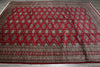 Load image into Gallery viewer, A large traditional oriental rug with a red diamond pattern and intricate geometric borders, laid out on a gray wood floor.